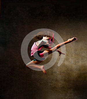 Street dance girl dancer jumping up dancing in neon light doing gymnastic exercises jump in studio on dark wall