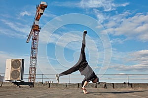 Street dancer hipster guy makes back flip with arm support on the roof outdoor.