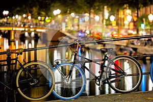 Street in the evening - bike and street lights, bridge and canal with reflection in the water. Romantic night scene of Amsterdam.