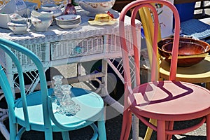 Street Fail Garage Sale Vintage Antique Dishes on Wicker Desk next to Colorful Wooden Brightly Painted Chairs photo