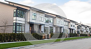 A street of family houses in suburban area with concrete side walk and asphalt road in front. Residential houses.