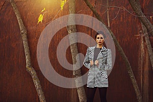 Street fashion concept. Fashion portrait of beautiful brunette in trendy casual clothes posing in autumn park over rusty metal