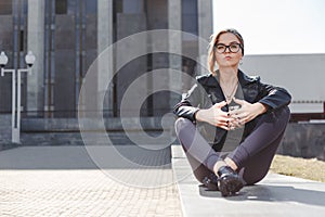 Street fashion concept - stylish cool girl in rock black style sitting among urban background outdoor