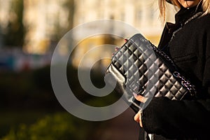 Street fashion concept. Woman in trendy coat holding black leather textured purse. Space for text