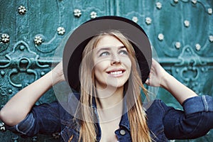 Street fashion portrait of a beautiful young lady smiling and looking up. Model wearing stylish wide-brimmed hat. City
