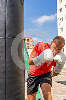 Street Fighter in Black Clothes and Bandages on the Wrist Boxing in Punching Bag Outdoors. Young Man Doing Box Training and