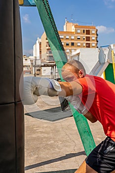 Street Fighter in Black Clothes and Bandages on the Wrist Boxing in Punching Bag Outdoors. Young Man Doing Box Training