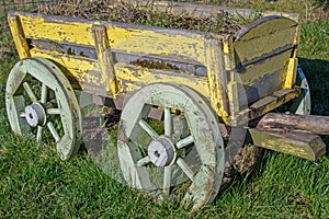 Street flower bed decorated in form of wood cart painted yellow with green wheels upholstered with metal strips, filled with earth