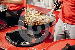 Street food chef cooking noodles and vegetables in a pan on fire at open kitchen. Fried noodles in a wok on the open fire. Asian