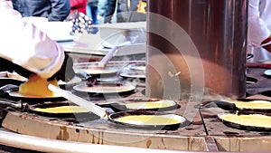 Street food. The cook cooks, fries, bakes pancakes in street cafe on frying pan at street fair, fast food. Chef preparing food