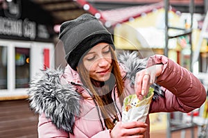 Street food. young woman holding greek meat gyros with tzatziki sauce, vegetables, feta cheese and french fries and eating oudoor photo