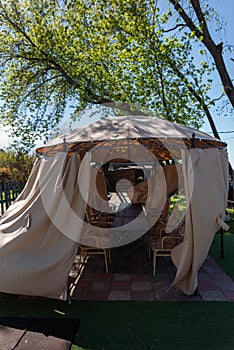 Street gazebo with a dome and light-colored curtains under a tree