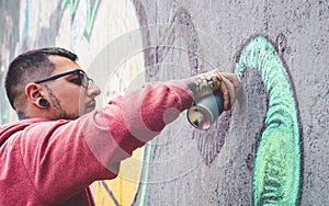 Street graffiti artist painting with a color spray can mural graffiti on the wall in the city