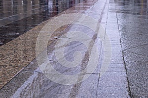 Street gutter with water flow on tiled sidewalk at rainy day. background, weather.