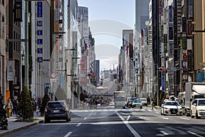 A street in a Japanese city with a dense building of tall modern houses and cars driving along a wide road. Tokyo, Japan, 2017-04-