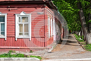 A street of Kaluga, Russia: an old red wooden house with white window frames, fresh green trees and couple in the distance