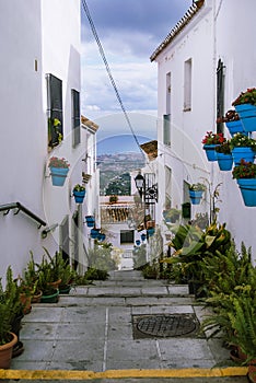 Street with ladders decorated with flowers and spots at white traditional spanish village Mijas