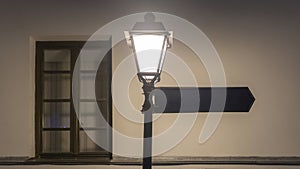 Street lamp with Blank Street Sign on empty wall background. Night time. Design concept