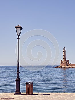 A street lamp and lighthouse in the port of Chania in Crete with a blue sea and sky in the background