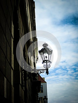 A street lamp that is mounted on the wall of the house against the backdrop of a dramatic sky