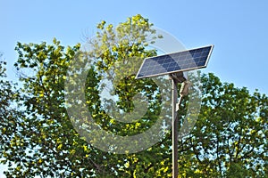 street lamp with a solar battery against a blue sky and trees