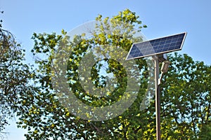 street lamp with a solar battery against a blue sky and trees