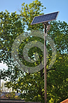 street lamp with a solar battery against a blue sky and trees