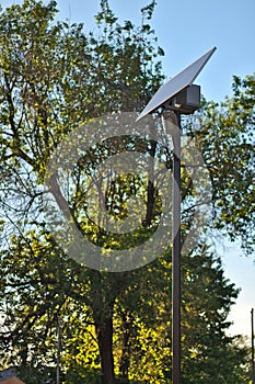 street lamp with a solar battery against a blue sky and trees
