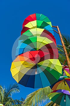 Street lamps decorated with colorful umbrellas hang on a pillar in street against the blue sky and coconut palm tree on a sunny