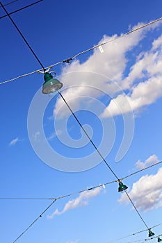 Street lamps on wires against cloudy blue sky