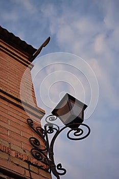 Street lantern made of black metal with forged curl pattern hang on the corner of house, blue sky background