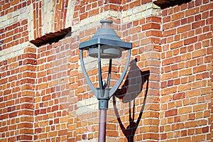 Street lantern street limp in bright sunlight with dark shadow on red brick wall
