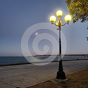 Street lantern with yellow light in the evening, lantern burns yellow light in the evening near the sea, romance near the lantern
