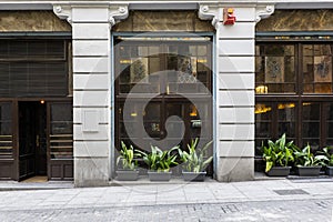 Street level entrance facade of an Irish pub style restaurant with potted plants and wooden storefronts