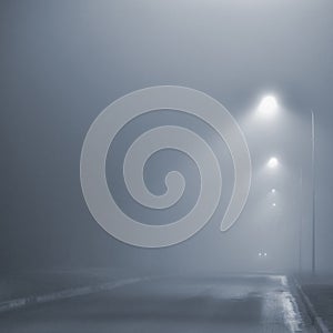 Street lights, foggy misty night, lamp post lanterns, deserted road in mist fog, wet asphalt tarmac, car headlights approaching