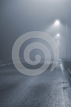 Street lights, foggy misty night, lamp post lanterns, deserted road in mist fog, wet asphalt tarmac, car headlights approaching