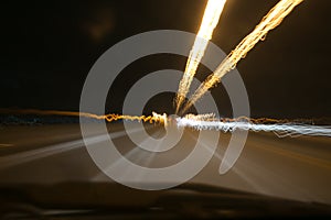 Street lights in speeding car in night time, light motion with slow speed shutter view from inside front of car.