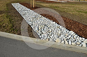 The street line is planted in a rectangular strip mulched by large white pebbles. clearer and more formal appearance than mulch ba