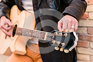 Street musician close up tuning the guitar. Fingers turning the tuning pegs of an acoustic guitar