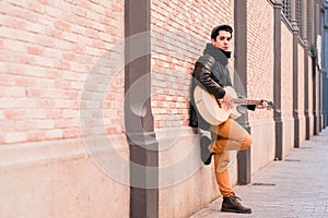 Street musician playing acoustic guitar. Young handsom man wearing coat and hat outdoors