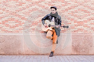 Street musician playing acoustic guitar. Young handsom man wearing coat and hat outdoors