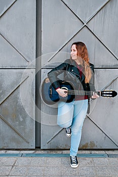 Street musician playing acoustic guitar. Young woman wearing jacket outdoors