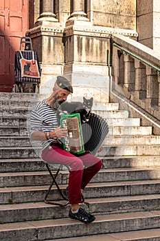 Street musician plays accordion with black cat in Paris, France