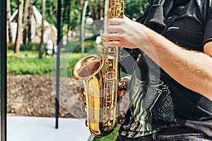 Street musician saxophonist plays jazz music in park in sunny day