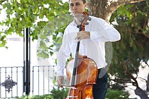 Street musician, young man playing cello in the street of big city, close up