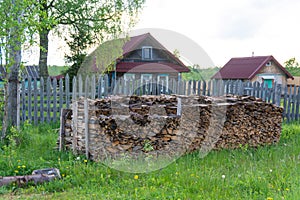 On the street near the house, firewood is neatly stacked under a tree.