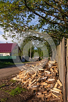 On the street near the house, firewood is neatly stacked under a tree.