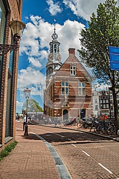 Street with people, brick buildings, steeple with golden clock and sunny blue sky in Amsterdam.