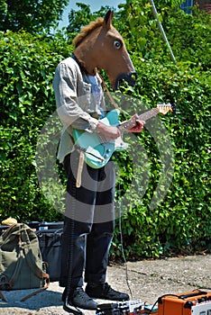 Street performer playing an electric guitar while wearing a horse head mask