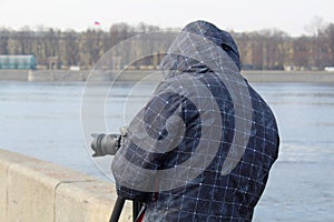 Street photographer in the process of shooting city landscapes. A camera on a tripod. A photographer in a jacket with a hood.